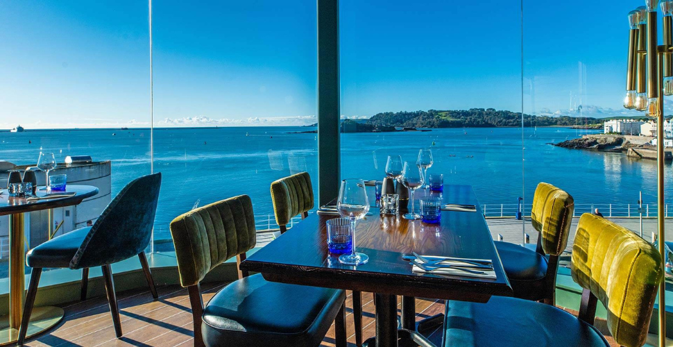 A table with glasses with a view of Plymouth Sound outside of the window